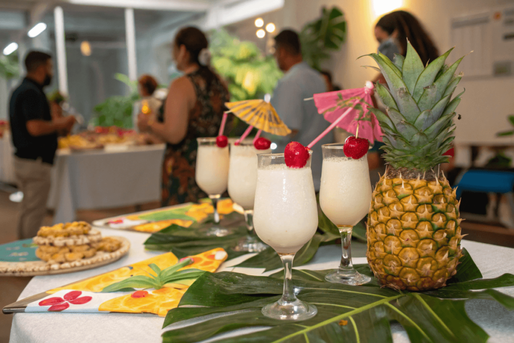 Party table with Virgin Piña Coladas garnished with pineapple and cherries, set against a festive tropical backdrop