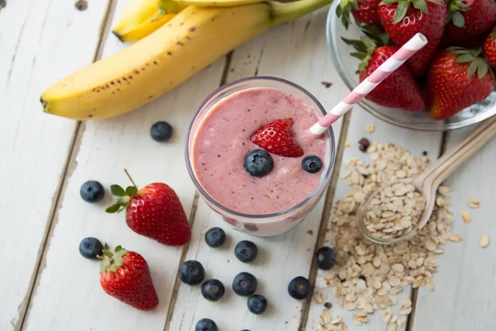 Strawberry blueberry banana smoothie in a clear glass with fresh fruit	